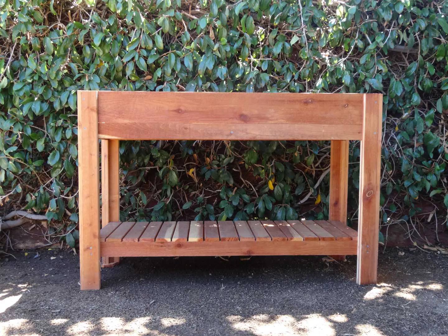 A wooden bench sitting in front of a bush.
