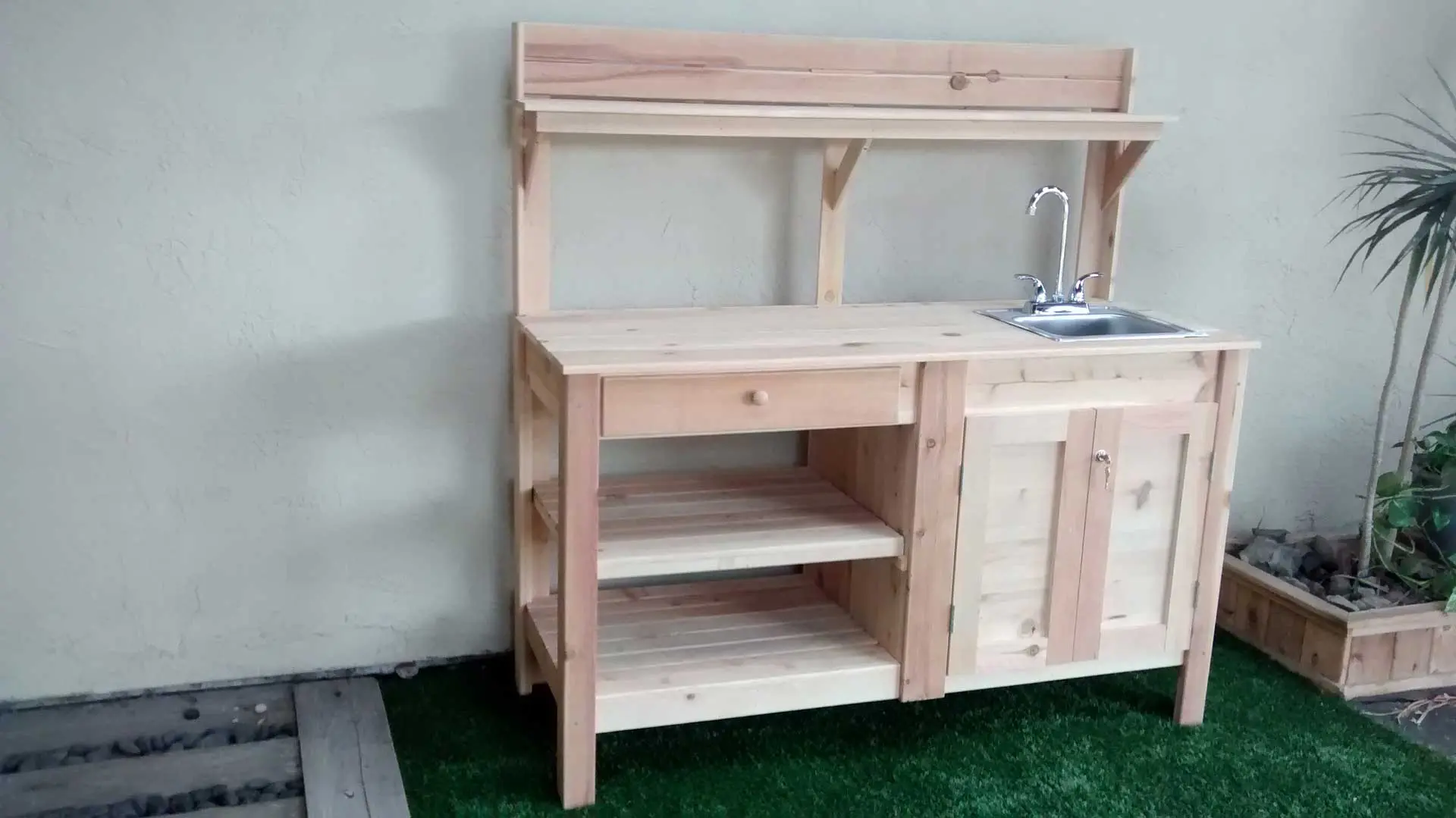 A wooden bench with sink and shelves on the side.