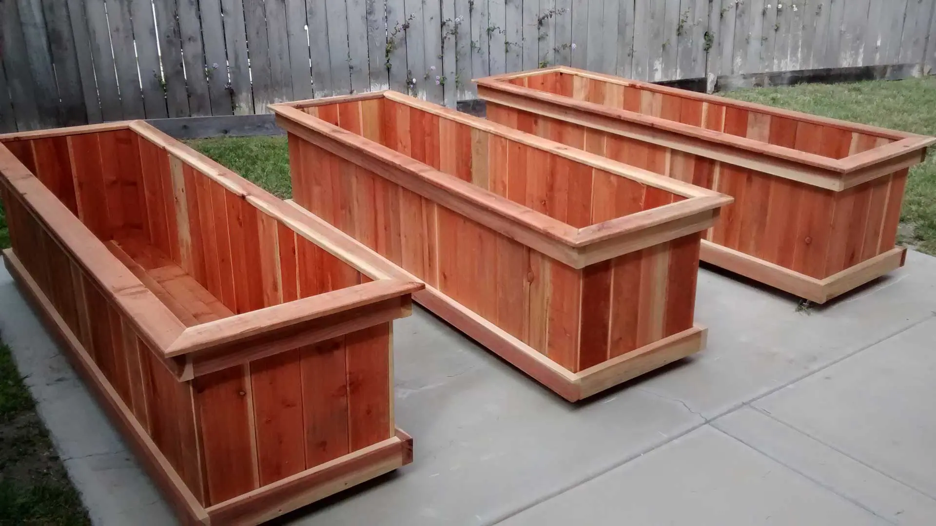 Three wooden planters on wheels in a backyard.