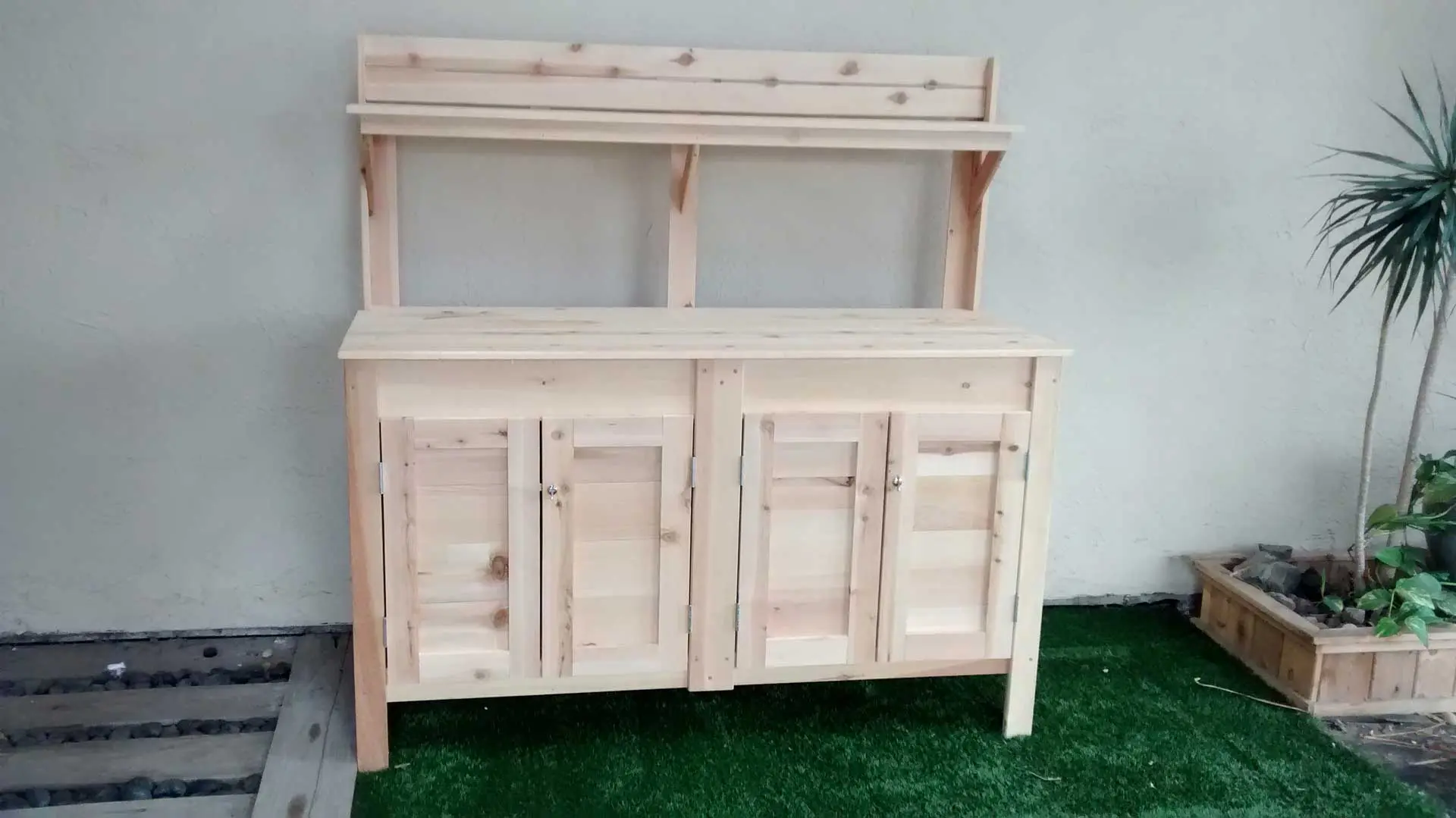 A wooden planter with two doors and two drawers.