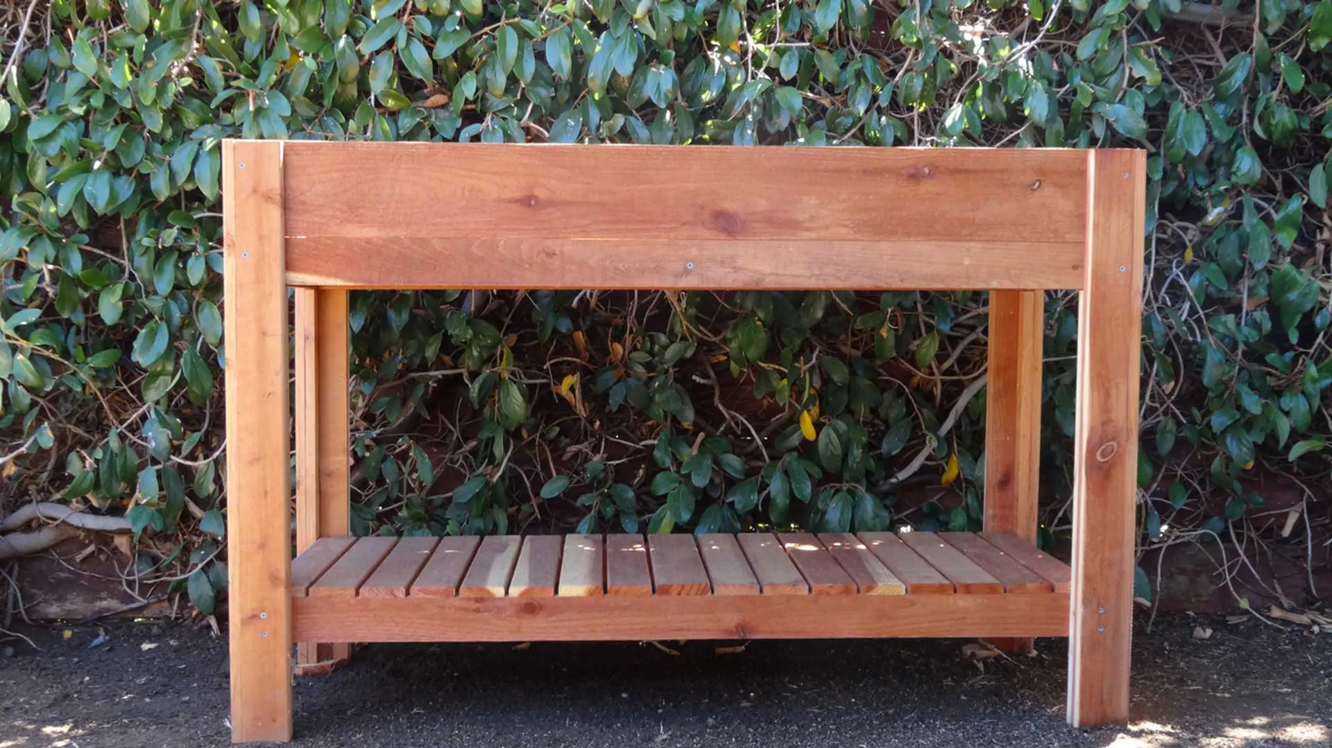 A wooden raised garden bed in front of bushes.