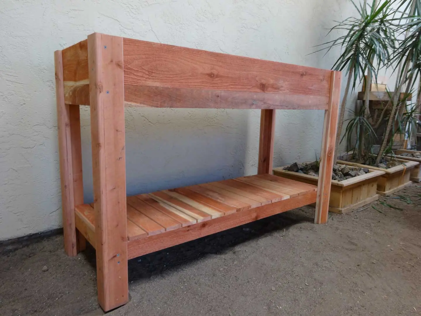 A wooden bunk bed with two levels and a plant in the corner.