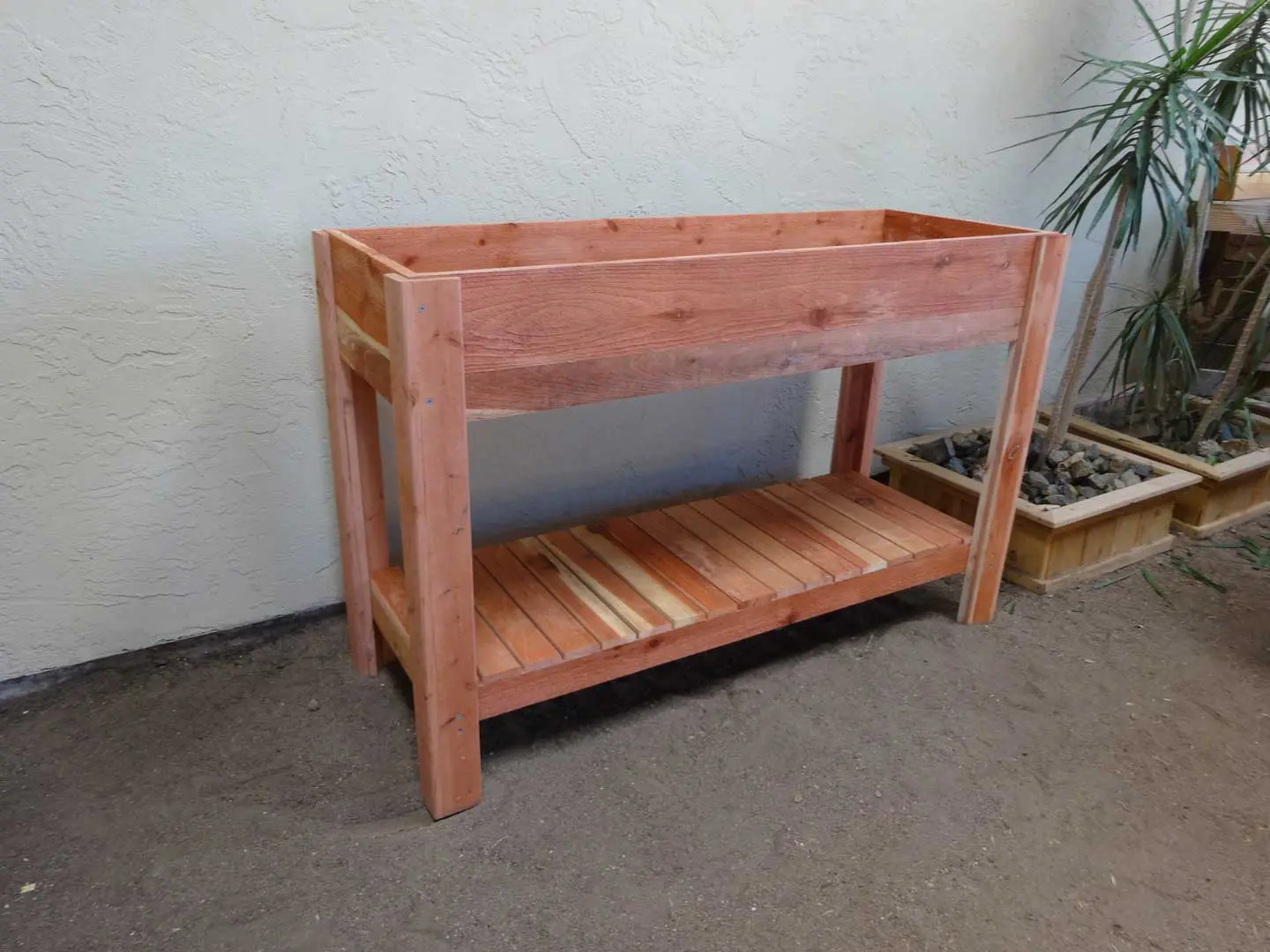 A wooden planter box with a shelf underneath it.