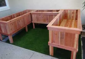 A wooden planter box with benches and artificial grass.