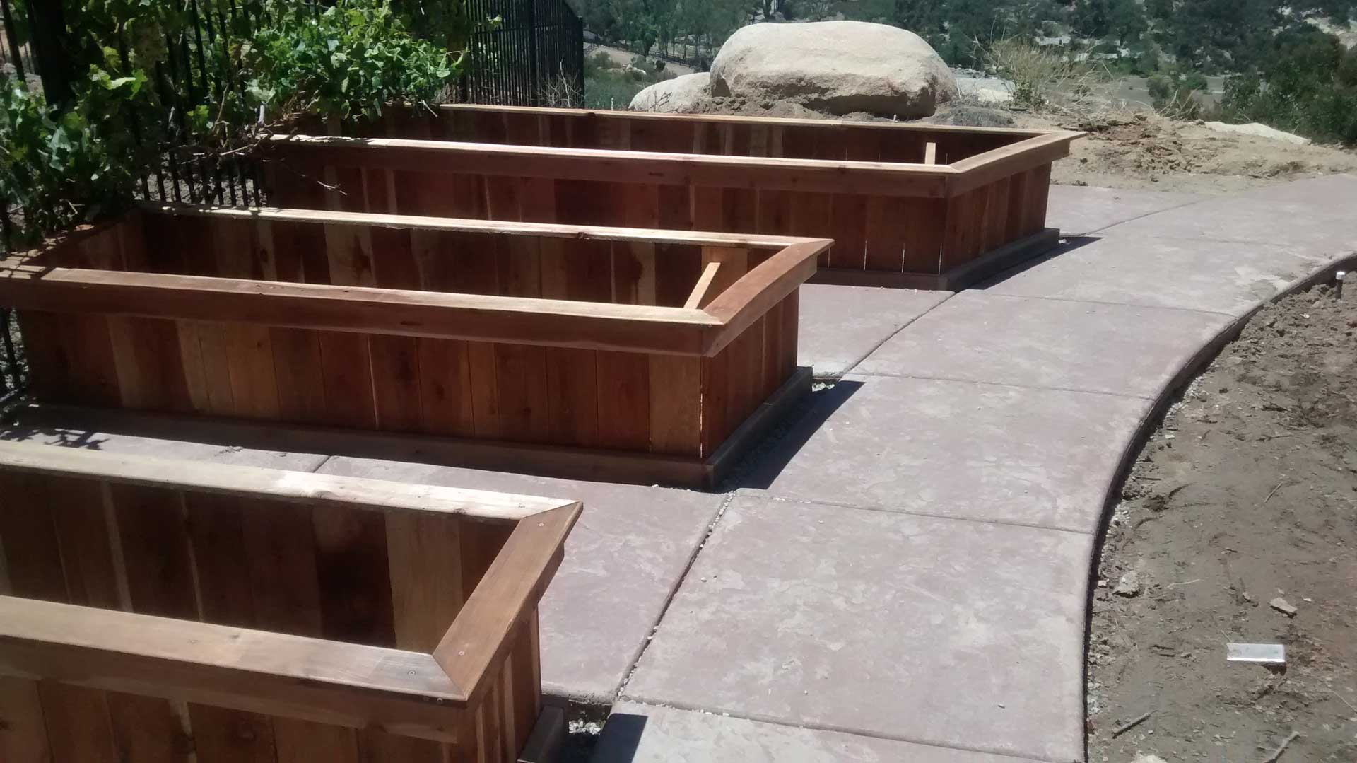Three wooden planters on the side of a sidewalk.
