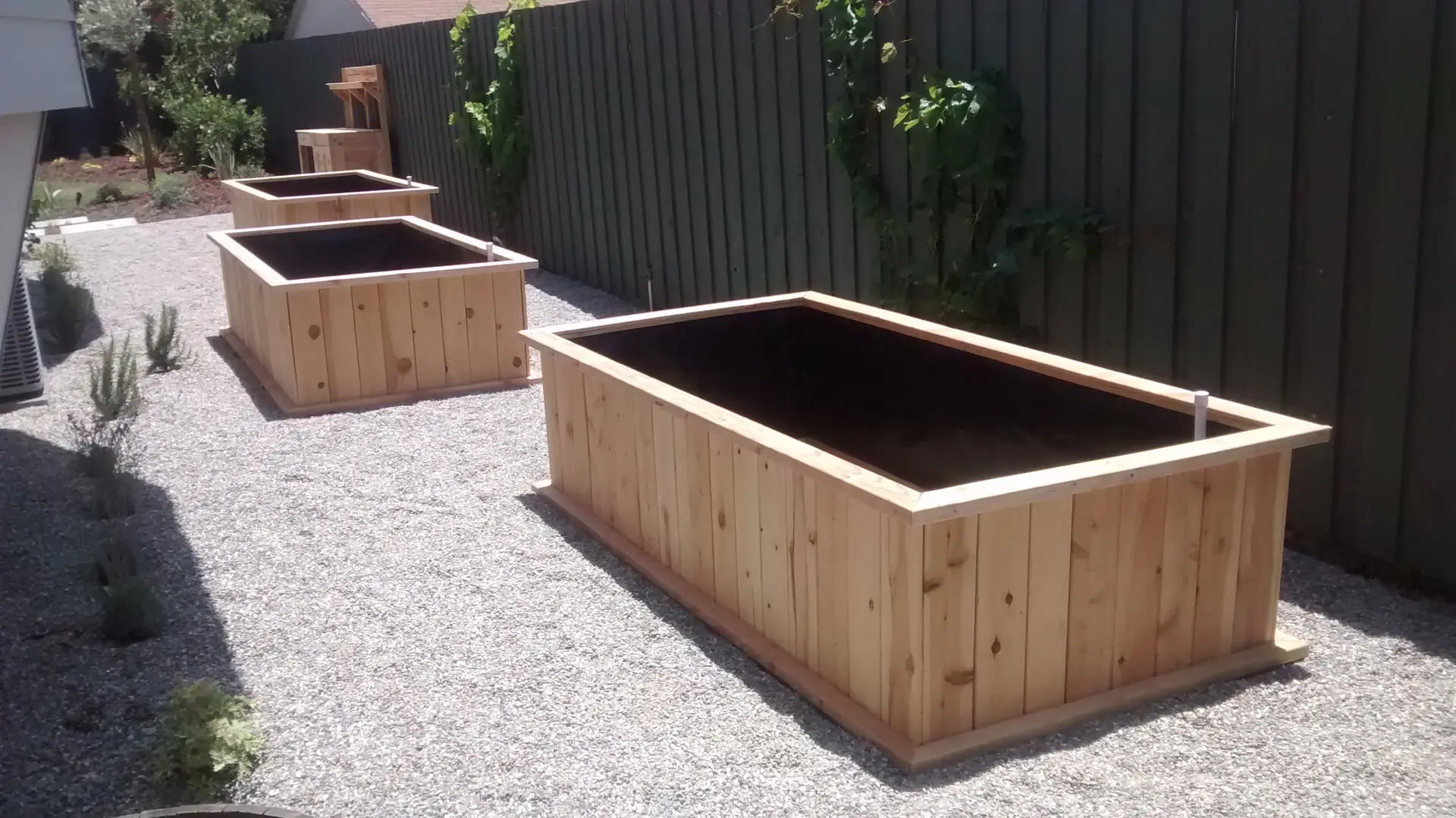 Three wooden planters in a gravel yard.