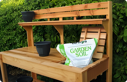 A wooden garden bench with a bag of soil.